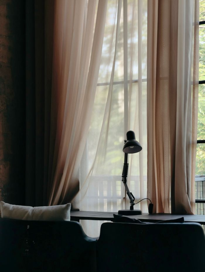 Sunlight streams through curtains onto a cozy workspace with a lamp in Haiphong, Vietnam.
